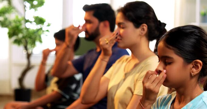 Indian young family doing meditation pranayama at home practicing breathing exercise together indoors during peaceful morning hours in a modern lavish living room promoting yoga health wellness