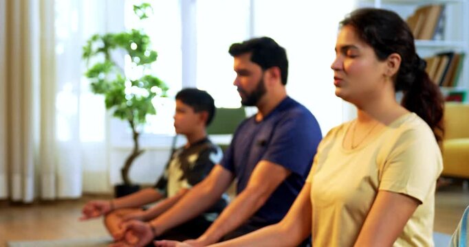 Indian young family doing omkar meditation pranayama at home chanting aum breathing yoga together indoors during peaceful morning hours in a modern living room promoting yogic lifestyle