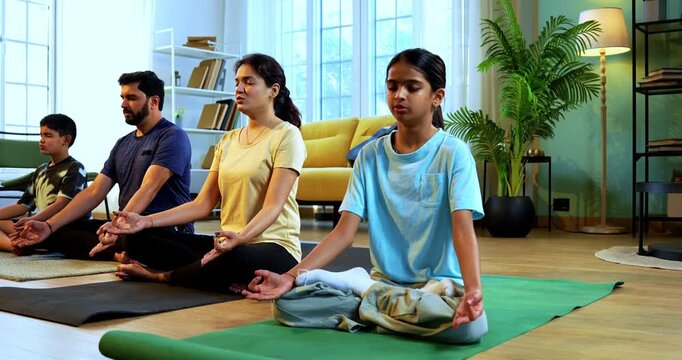 Indian young family doing omkar meditation pranayama at home chanting aum breathing yoga together indoors during peaceful morning hours in a modern living room promoting yogic lifestyle