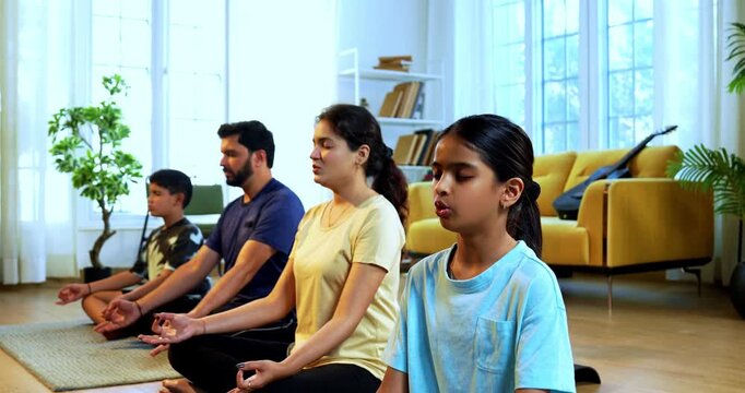 Indian young family doing omkar meditation pranayama at home chanting aum breathing yoga together indoors during peaceful morning hours in a modern living room promoting yogic lifestyle