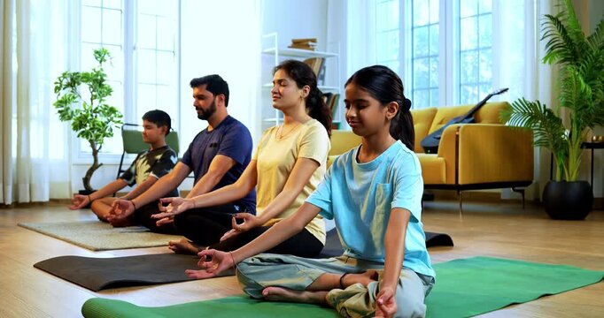 Indian young family doing omkar meditation pranayama at home chanting aum breathing yoga together indoors during peaceful morning hours in a modern living room promoting yogic lifestyle