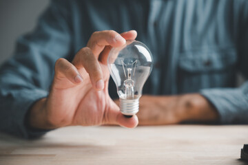 A hand holds a lightbulb over a wooden table, symbolizing new ideas and innovation.