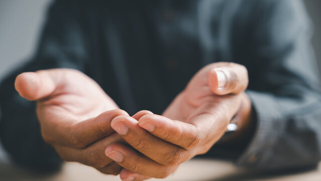 Close-up of open hands with fingers extended, palms up, in a gesture of offering or receiving.  The background is blurred and dark.  A symbol of hope and giving.