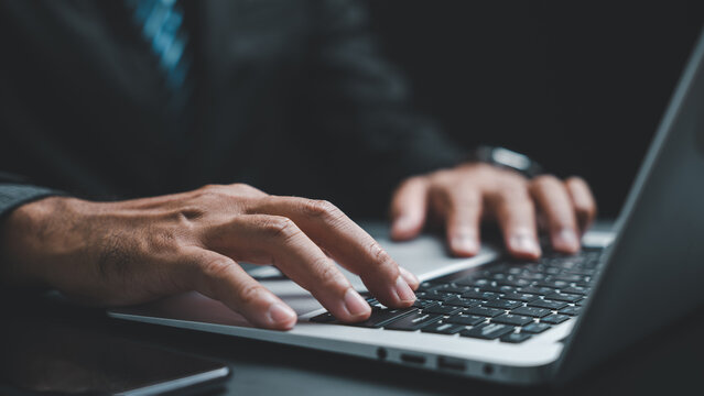 Close-up of hands typing on a laptop keyboard. The image focuses on the hands and the keyboard, with a blurry background.