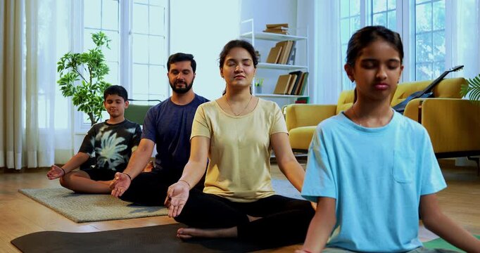 Indian young family doing omkar meditation pranayama at home chanting aum breathing yoga together indoors during peaceful morning hours in a modern living room promoting yogic lifestyle