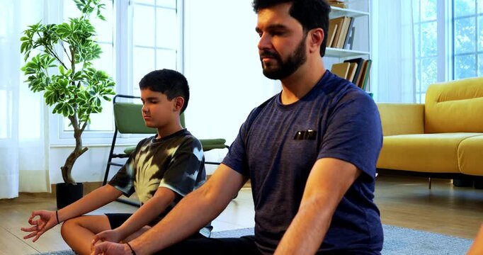 Indian young family doing omkar meditation pranayama at home chanting aum breathing yoga together indoors during peaceful morning hours in a modern living room promoting yogic lifestyle