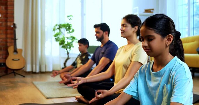 Indian young family doing omkar meditation pranayama at home chanting aum breathing yoga together indoors during peaceful morning hours in a modern living room promoting yogic lifestyle