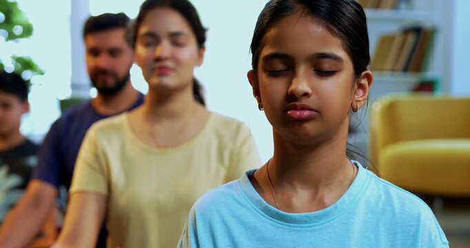 Indian young family doing omkar meditation pranayama at home chanting aum breathing yoga together indoors during peaceful morning hours in a modern living room promoting yogic lifestyle