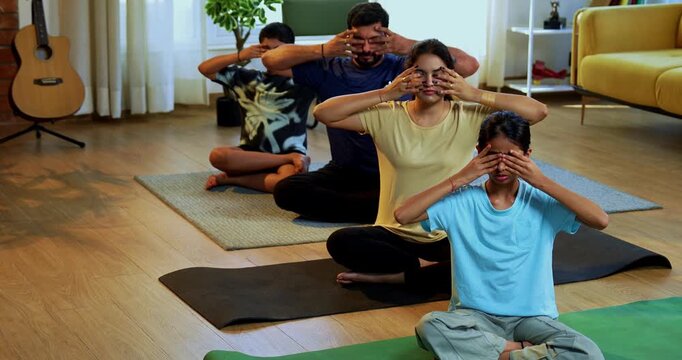 Indian family of four bhramari pranayama or bee breathing exercise practicing yogic breath together indoors during calm morning hours inside a modern home promoting health wellness in yogic style