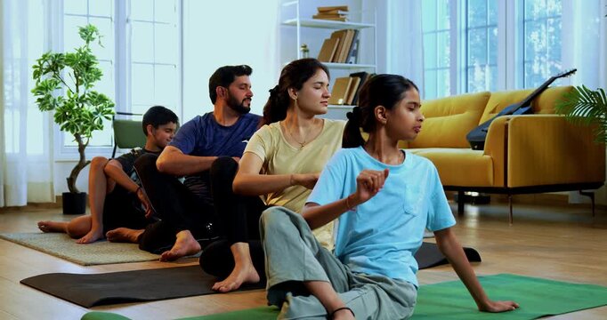 Indian family doing yog asana at home practicing ardha matsyendrasana seated spinal twist yoga together indoors during calm morning hours inside a modern lavish living space promoting health