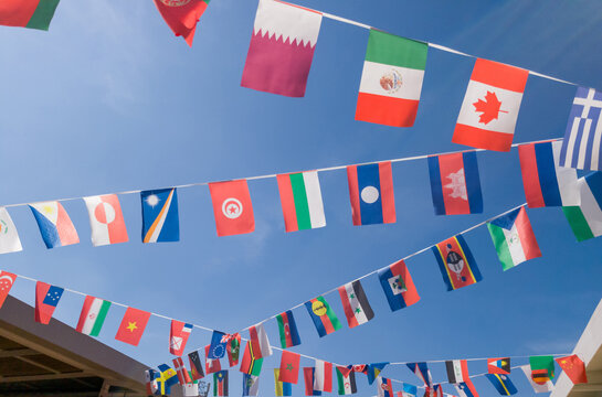 International flags from various nations hang on bunting lines against clear vibrant blue sky. Perfect for global themes multicultural events and world unity celebrations