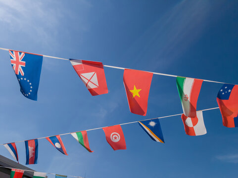 International flags from various nations hang on bunting lines against clear vibrant blue sky. Perfect for global themes multicultural events and world unity celebrations