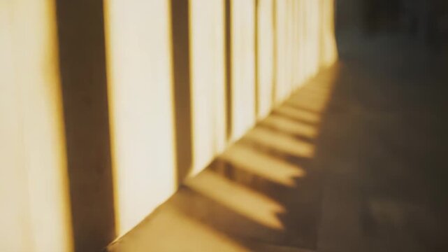 Golden sunlight casts strong parallel shadows from an unseen element onto a textured beige wall and floor, creating a warm, abstract pattern of light and dark stripes