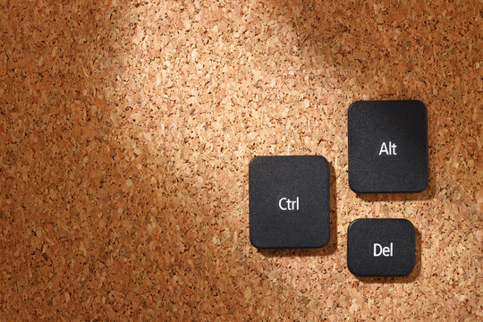 Black keyboard keys "Ctrl", "Alt", "Del" on a cork bulletin board in soft sunlight, symbolizing the classic computer reboot shortcut. Top view.