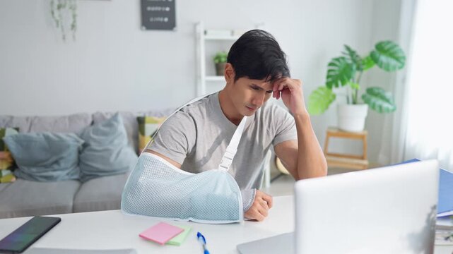 Injured Asian businessman wearing hand splint while working from home. 