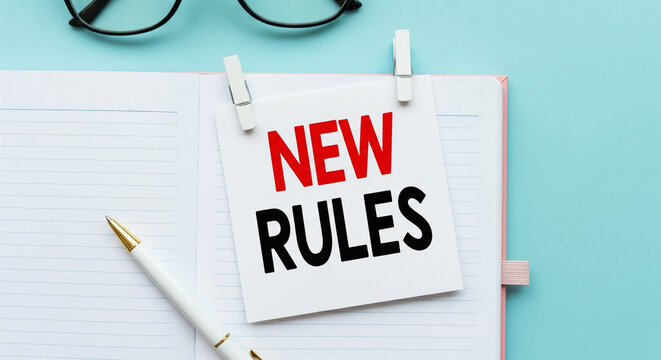 New rules sign pinned on notebook with pen and glasses on blue background