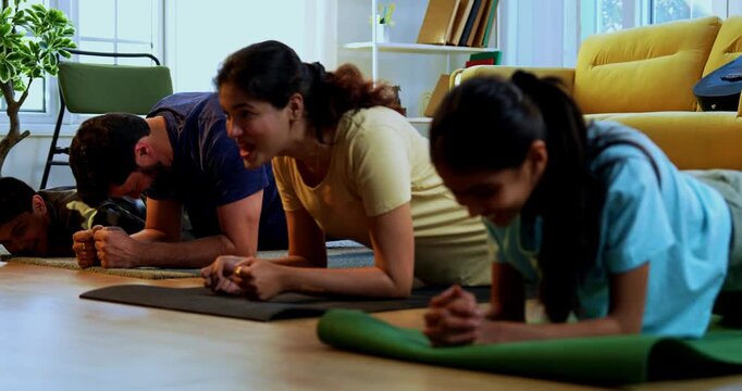Indian family doing plank exercise at home practicing core strength together with lighthearted mood indoors on floor during family fitness session in a modern lavish living space promoting health