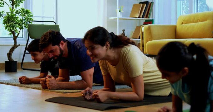 Indian family doing plank exercise at home practicing core strength together with lighthearted mood indoors on floor during family fitness session in a modern lavish living space promoting health