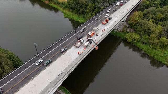 Drone aerial over Vilnius, Lithuania showing a river overpass under bridge repair and roadworks, with crews, lane closure, and traffic moving through a work zone.