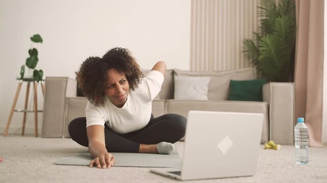Woman doing yoga at home, watching online workout by laptop, feel pain in knee. Young adult housewife training alone in apartment and get trauma of knee-joint, independent sport activity, home fitness