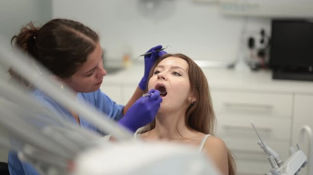 Young woman came for an examination and professional dental hygiene at a dental clinic. Woman dentist carefully examines the teeth of a client. High quality 4k footage