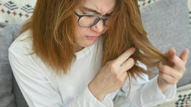 Asian woman holding and checking her damaged split ended hair. Hair damage is risk for further damage and breakage. It may also look dull or frizzy and be difficult to manage.