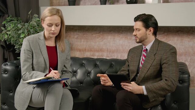 Confident successful handsome male team leader with digital tablet giving job task to attractive female colleague, discussing business matters and planning strategy at office