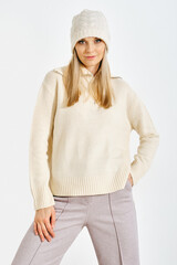 Model poses in a sweater and hat during a fashion shoot in a studio setting in daylight