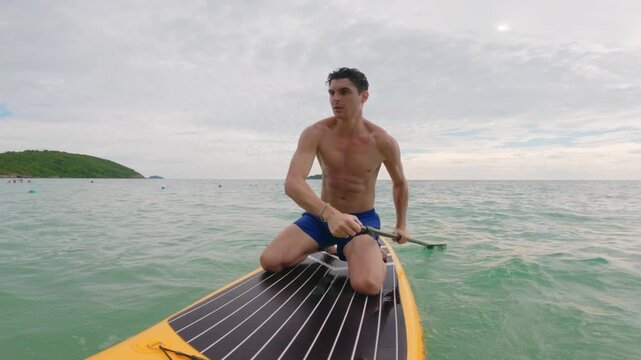 Caucasian young man rows on a paddleboard as glides over the ocean waves.