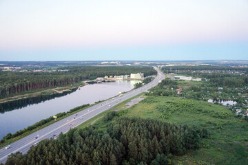 Highway with traffic near forest and lake at dusk aerial view