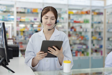 Smiling female pharmacist using digital tablet wearing headset. Young healthcare professional...