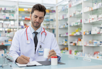 Male healthcare professional writing notes while holding medicine bottle. Confident doctor or...