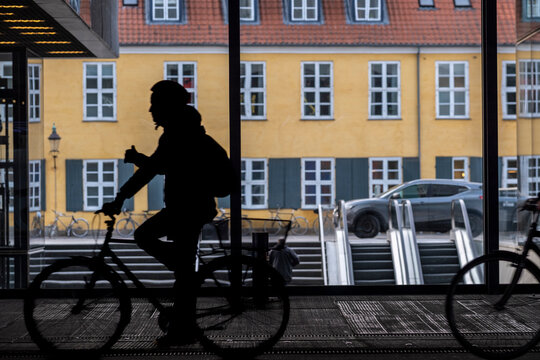 Backlit cyclist silhouette on bicycle along urban street in Copenhagen Denmark capturing city commute and everyday transport culture