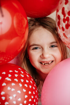 Smiling girl surrounded by red and pink Valentine's balloons