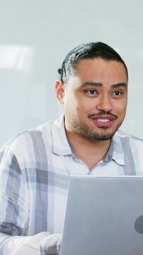 Vertical video: After laptop ping man in striped shirt smiling, typing, looking left at desk