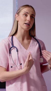 Vertical video: Recording medic in pink scrubs explaining wrist care in clinic with steth