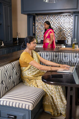 Indian mother and daughter typing and cooking in home kitchen with laptop and stove © wavebreak3
