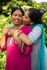 Indian mother and daughter hugging and kissing cheeks in garden with embroidered kurta © wavebreak3