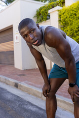 Obraz premium African american man crouching by curb beside house in tank top, shorts, smartwatch, sweating