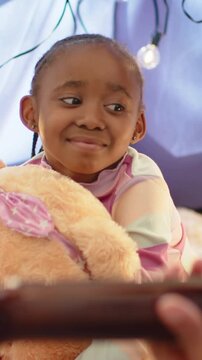 Vertical video: Hand showing phone, girl reaching for phone in tent, holding plush bear, pastel top