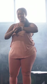 Vertical video: Smiling woman in pink leggings stepping, checking smartwatch after alert at gym