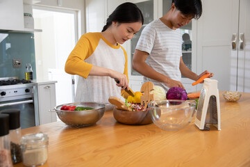 Asian couple slicing bell pepper into salad bowl and peeling carrots on home kitchen island © wavebreak3