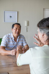 Obraz premium Senior couple sitting opposite at table in home with framed artwork and intercom