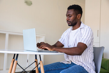 African american man typing on laptop at white table in home office, copy space