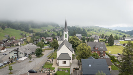 Fototapeta premium Aerial drone view of Wildhaus, a small town, in the Swiss Alps, Alpstein region. Churches and houses, cloudy summer day. Swiss travel destination. Outdoor hiking destination in pristine alps.