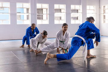 Diverse martial artists performing lunges wearing gis and belts on black mats in dojo