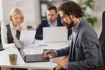 Fototapeta premium Team members are focused on their tasks in a bright office space. One person types on a laptop while others share ideas and documents, contributing to their work.