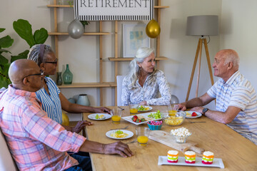 Obraz premium Diverse senior friends chatting at home dining table with fruit, juice under retirement banner