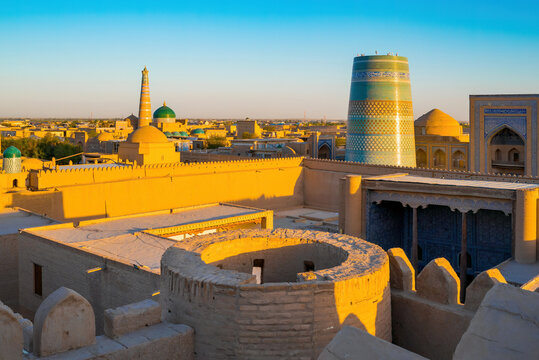 High angle view of Khiva old town, Uzbekistan, featuring Kalta Minor minaret at sunset. Ancient citadel with turquoise tiles and clay domes in golden light