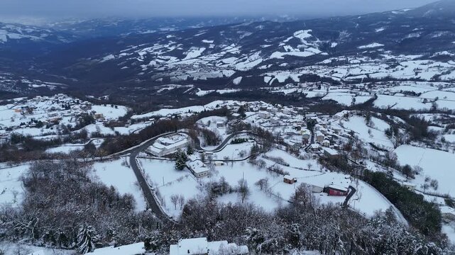 Wide drone panorama of Le Bore village and snow valley and winding rural roads, Valmozzola, Italy